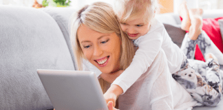 A woman on the computer with a child on her back.