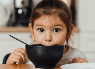 A girl putting her mouth on a black bowl.
