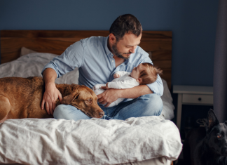 A dad holding a baby and a dog.
