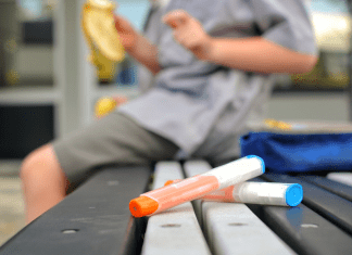 A kid eating while sitting next to an epipen.