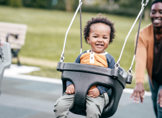 A mom pushing her toddler on a swing.
