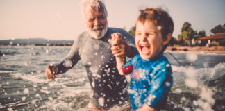A grandfather playing with his grandson in the ocean.