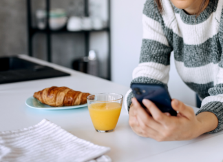 Meet Julie: Daily Chaos A woman checking her phone in the kitchen with breakfast.