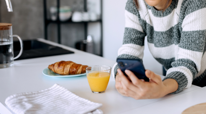 A woman checking her phone in the kitchen with breakfast.