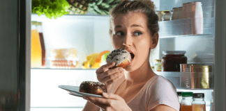 A woman eating donuts in front of the refridgerator.