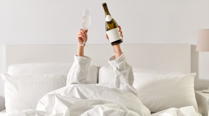 A woman holding champagne in a hotel bed.