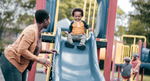 A mom at the playground watching her son on the slide.