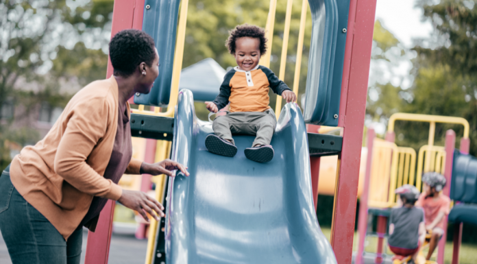 A mom at the playground watching her son on the slide.