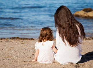 A teacher mom and daughter sitting on the beach.