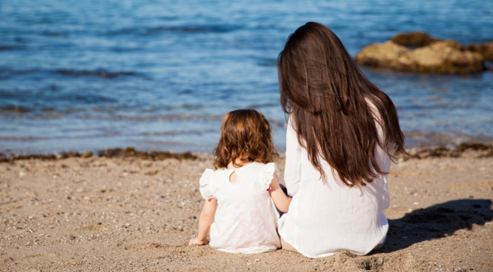 A teacher mom and daughter sitting on the beach.