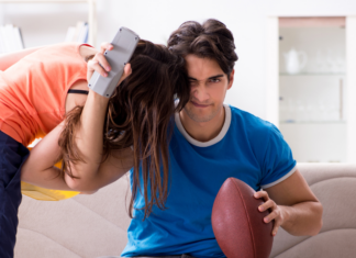 A man watching a football game while his wife tries to get attention.