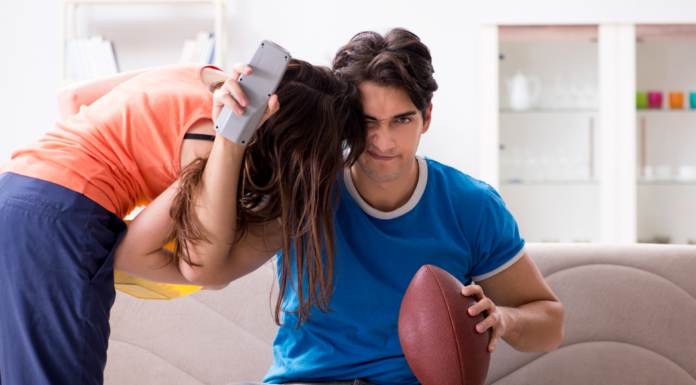 A man watching a football game while his wife tries to get attention.