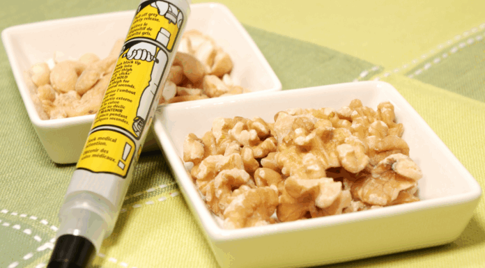 An epi pen next to a bowl of walnuts.