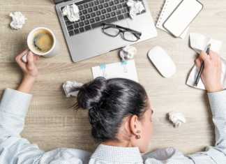 A stressed woman with her head down on her computer with ripped paper all around.