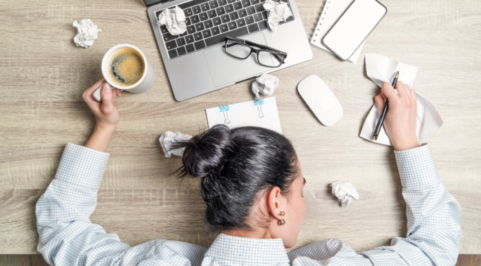 A stressed woman with her head down on her computer with ripped paper all around.