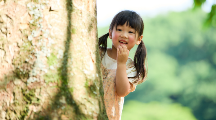 An introverted girl hiding behind a tree.