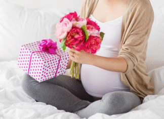 A pregnant woman holding flowers and a gift.