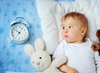 A toddler in bed next to a sleep clock.