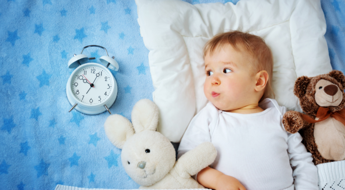 A toddler in bed next to a sleep clock.