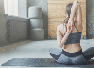A woman sitting on a yoga mat doing a back stretch.