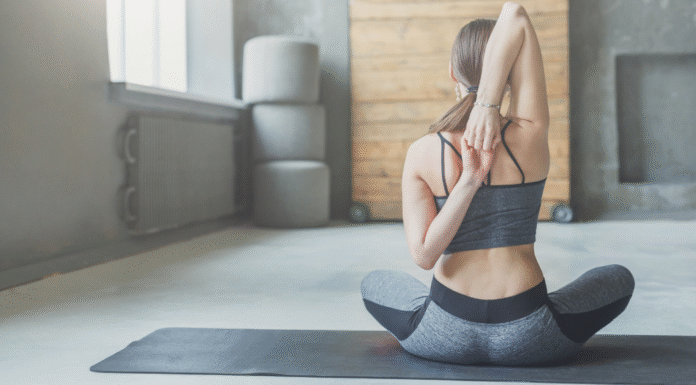 A woman sitting on a yoga mat doing a back stretch.