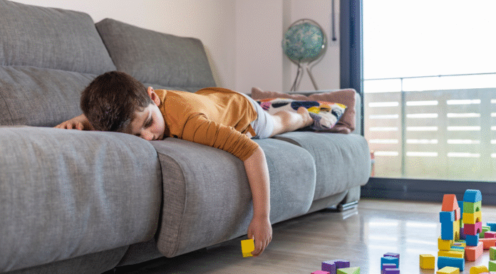 A boy laying on the couch bored.