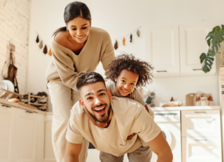 A boy riding on his dad's back while mom helps.