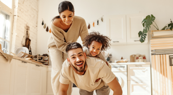 A boy riding on his dad's back while mom helps.