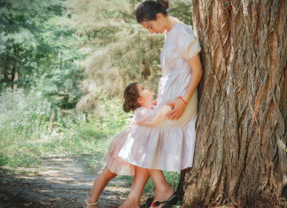 A mother leaning against a tree looking at her daughter.