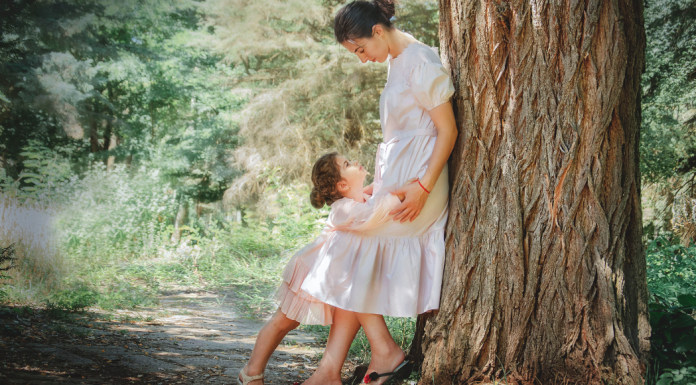 A mother leaning against a tree looking at her daughter.