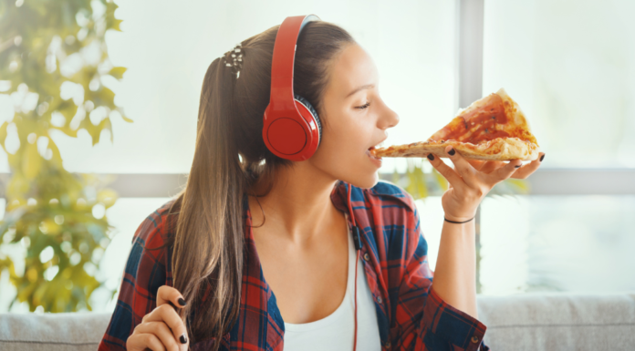 A girl eating pizza listening to headphones.