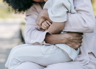 A woman's arms wrapped around her child on a park bench.