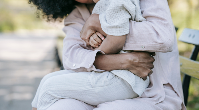 A woman's arms wrapped around her child on a park bench.