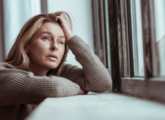 A sad woman looking out the window during winter.