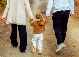 A toddler walking and holding hands with parents.