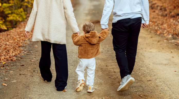 A toddler walking and holding hands with parents.