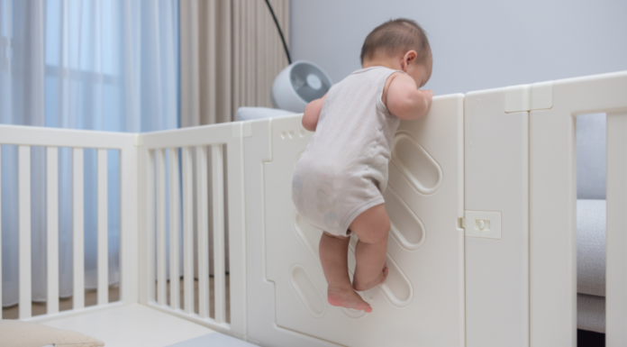 A baby climbing out of a crib.