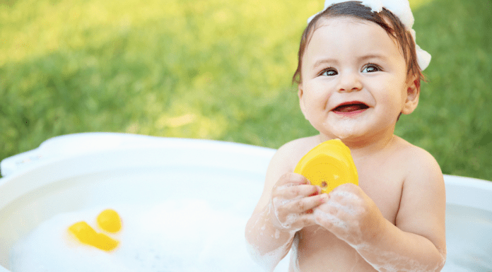 A toddler sitting in a tub holding a rubber ducky.