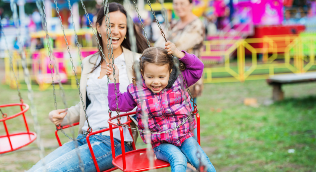 A mother and daughter on a swing ride at a fall festival. 