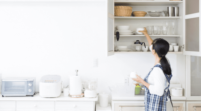 A woman putting items in a kitchen shelf.