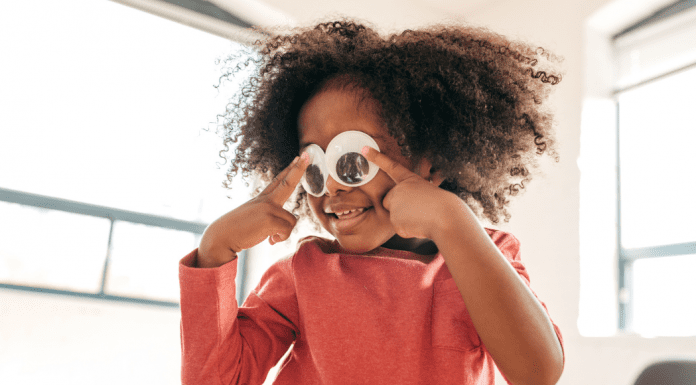 A young girl holding up googly eyes.