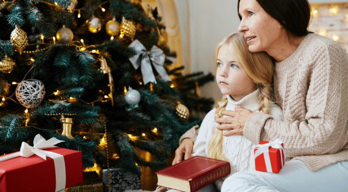 A mom holding a little girl in front of the Christmas tree.