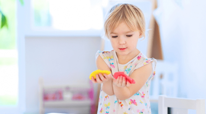 A toddler holding yellow and red play dough.