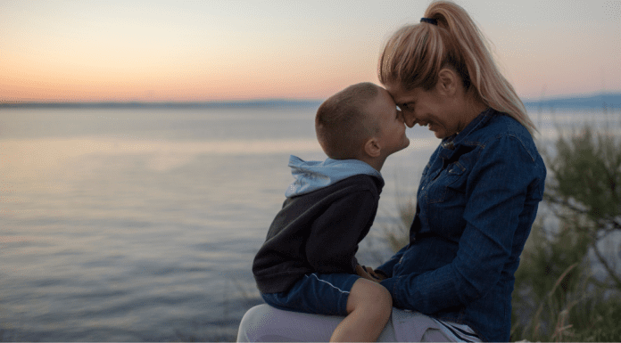 A son sitting on his mother's lap and kissing her nose.
