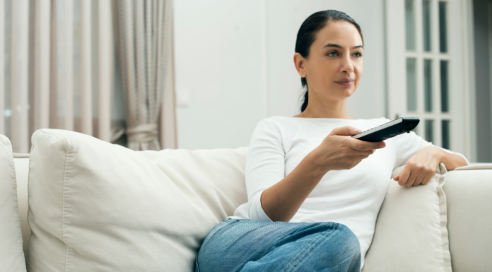A woman holding a TV remote while sitting on the couch.