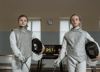 Two girls dressed in fencing gear.