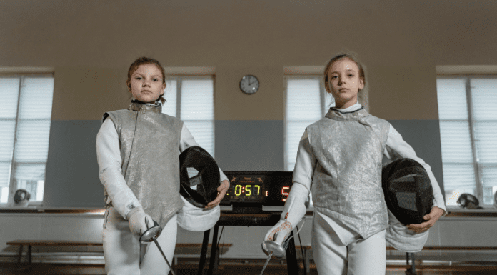 Two girls dressed in fencing gear.