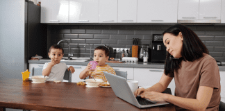 A mom working while her kids eat breakfast during the summer.