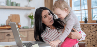 A woman holding a child reaching for a computer.