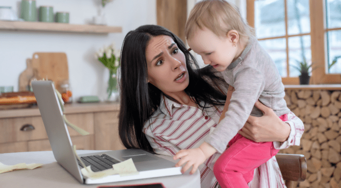 A woman holding a child reaching for a computer.